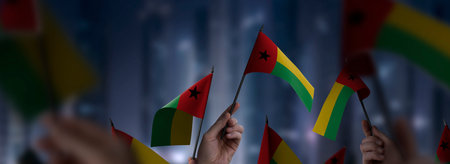 Guinea Bissau flags in their hands on a blurred urban background. The photo illustration was created without the use of artificial intelligence, only using Photoshop.の写真素材