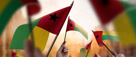 Guinea Bissau flags in their hands on a blurred urban background. The photo illustration was created without the use of artificial intelligence, only using Photoshop.の写真素材