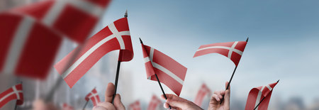 Denmark flags in their hands on a blurred urban background. The photo illustration was created without the use of artificial intelligence, only using Photoshop.の写真素材