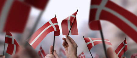 Denmark flags in their hands on a blurred urban background. The photo illustration was created without the use of artificial intelligence, only using Photoshop.の写真素材