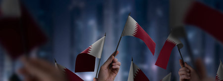 Qatar flags in their hands on a blurred urban backgroundの写真素材