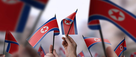 North Korea flags in their hands on a blurred urban backgroundの写真素材