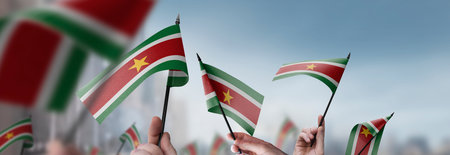 Suriname flags in their hands on a blurred urban backgroundの写真素材
