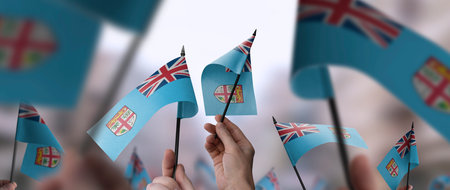 Fiji flags in their hands on a blurred urban backgroundの写真素材