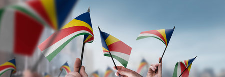 Seychelles flags in their hands on a blurred urban backgroundの写真素材