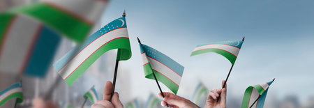 Uzbekistan flags in their hands on a blurred urban backgroundの写真素材