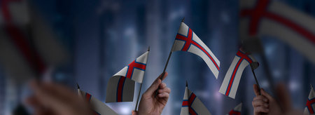 Faroe Islands flags in their hands on a blurred urban background