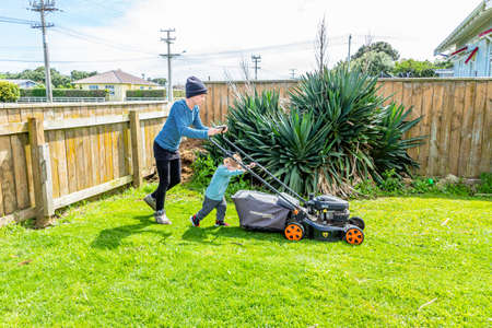 Son helpw mother push the lawn mower while  mowing the lawnTaranaki, New Zealand