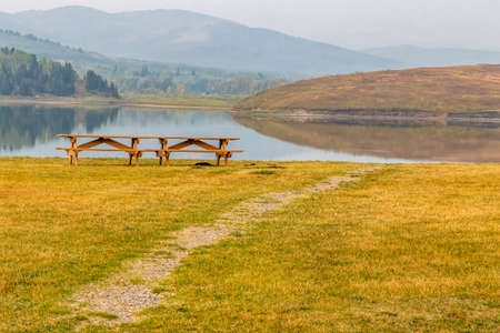 Picnic tables and bench sit alone by waters edge. Chain Lakes Provincial Park, Alberta, Canada