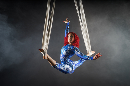 athletic sexy aerial circus artist with redhead in blue costume dancing in the air with balanceの写真素材