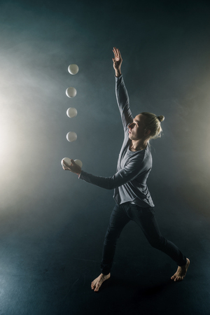 Blond juggler with white balls on black backgroundの写真素材