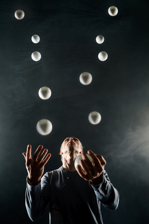 Blond juggler with white balls on black backgroundの写真素材