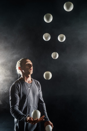Blond juggler with white balls on black backgroundの写真素材