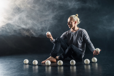 Blond juggler sitting on the floor with white balls on black backgroundの写真素材