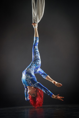 athletic sexy aerial circus artist with redhead in blue costume making tricks on the aerial silkの写真素材