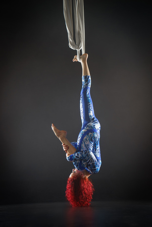 athletic sexy aerial circus artist with redhead in blue costume making tricks on the aerial silkの写真素材