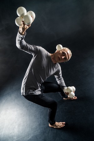 Blond juggler with white balls on black backgroundの写真素材