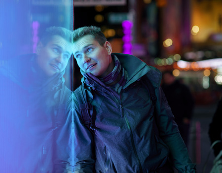 Stylish young man with his reflection on background with blurred lights of the city at nightの写真素材