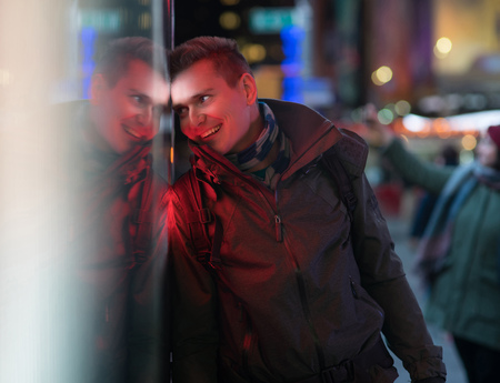 Stylish young man with his reflection on background with blurred lights of the city at nightの写真素材