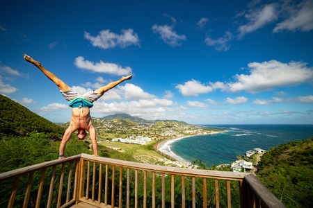 Young man standing on hands on the edge with panoramic view of mountain sea and skyの写真素材