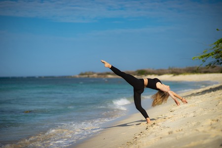 Blond young girl wearing black tights doing dancing poses on the beach. Summer day and happy holiday...