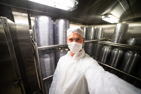 Young man taking selfie in restaurant kitchen storage room with stacks of plates, on metal shelves