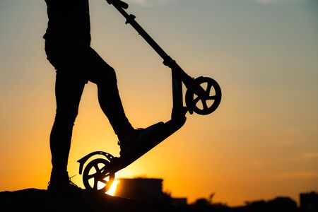 silhouette of a person holding kick scooter with beautiful sunrise on background close upの写真素材
