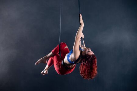 Female athletic, sexy and flexible aerial circus artist with redhead on aerial straps on black backgroundの写真素材