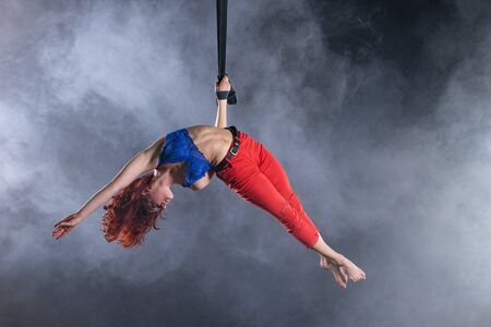 Female athletic, sexy and flexible aerial circus artist with redhead on aerial straps on black backgroundの写真素材