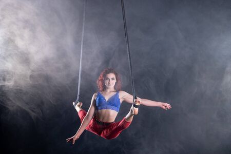 Female athletic, sexy and flexible aerial circus artist with redhead on aerial straps on black...