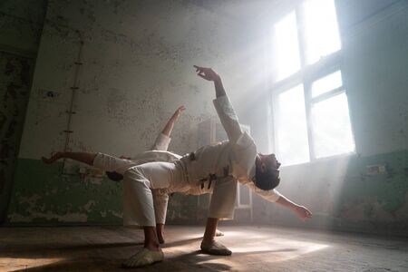 Male duo making acrobatic tricks wearing costume of insane people in abandoned room with sun rays from windowsの写真素材