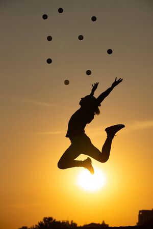 Silhouette of juggler jumping with balls on colorful sunsetの写真素材