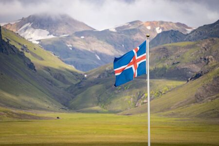 Flag of Iceland against the background of green mountains and blue skyの写真素材