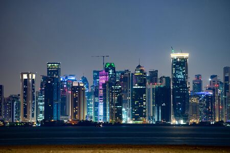 Vibrant Skyline of Doha at Night as seen from the opposite side of the capital city bay sunset.
