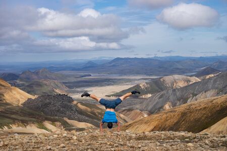 Hiker standing on his hand in the Landmannalaugar Valley. Iceland. Colorful mountains on the...