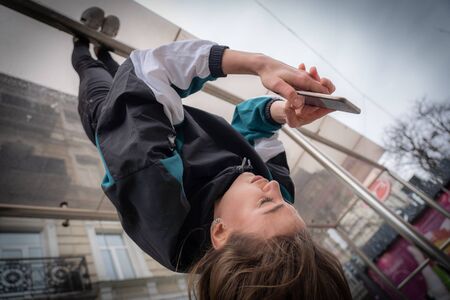 Girl hanging by feet upside down in the street and using smartphone. Concept of overusing social...