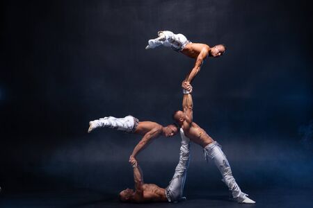 Four muscular man perform difficult acrobatic tricks on black studio.の写真素材