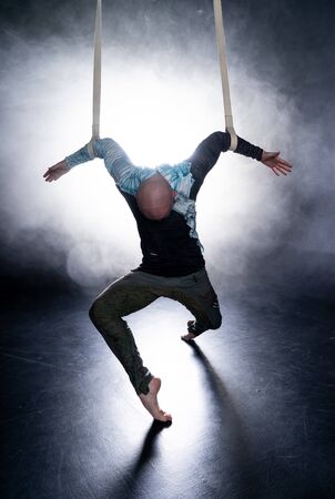 Circus artist on the aerial straps with costume on the black and smoked background. Concept of suffering, despair and defeat.の写真素材