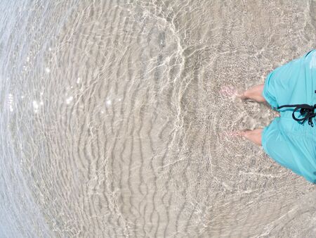 Male Feet standing on the shallow crystal Sea Water Beach Sand. Concept of relsx and happiness
