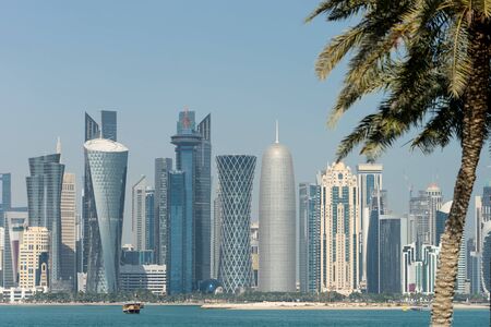 Panoramic view of modern skyline of Doha through blurred palm trees. Qatar on sunny day.
