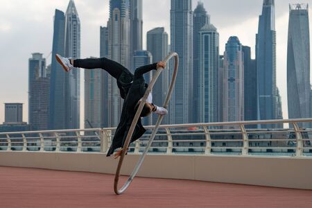 Cyr Wheel artist wearing black and white smart clothes with cityscape background of Dubai during sunset.の写真素材