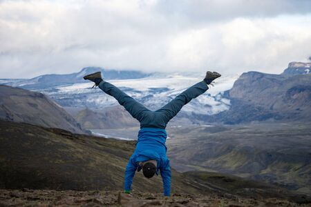 young guy standing on his hands with snowy mountain and glacier background on the way of Laugavegur...