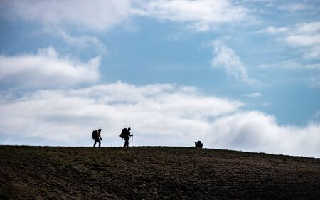 Silhouettes of people walking with backpacks on the sky backgroundの写真素材