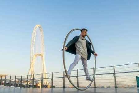 Dubai, February 2020. Cyr Wheel artist with Ferris wheel on background of Dubai during sunsetのeditorial素材