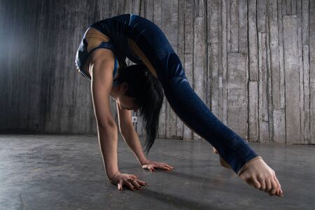 Young female Acrobat Standing on Hand over gray background in photo studio. Flexible Woman Circus...