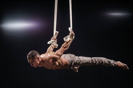 circus artist on the aerial straps with Strong muscles on black backgroundの写真素材