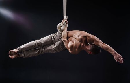 circus artist on the aerial straps with Strong muscles on black backgroundの写真素材