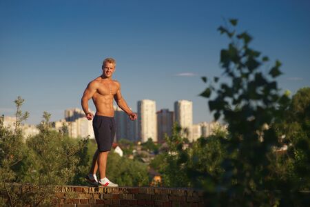Muscular young man standing on top of the roof and looking at during sunset. Concept of healthy lifestyle and confidentの写真素材