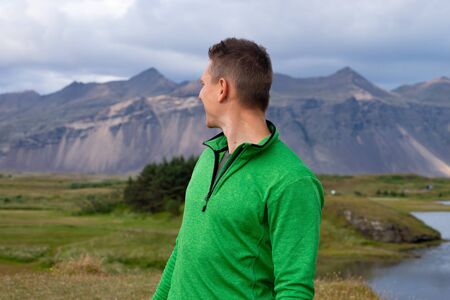 Backside of tall caucasian man wearing green jacket standing in over mountain and fog background. Promoting healthy lifestyleの写真素材