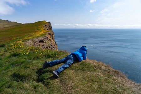 The man lying on Latrabjarg cliff and looking down.